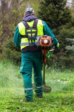 Yeşil bir çevrede çim biçme makinesini koruyucu ekipmanlarla çalıştıran biri.