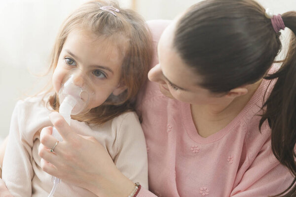 Женщина с дочерью делают вдох с распылителем в своей спальне дома