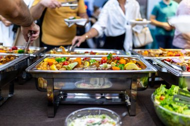 Misafirler keyifli bir şekilde çeşitli yemekler, sebzeler ve taze salatalar da dahil olmak üzere renkli bir büfeden servis ederken, ortak bir atmosferde sosyalleşiyorlar..