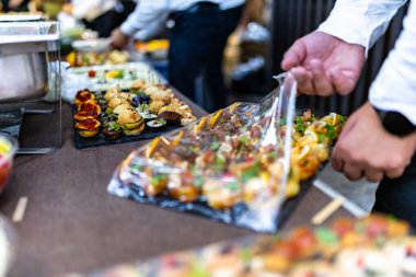 Canlı bir etkinlikte, bir yemek firması konuklar kaynaşırken çeşitli aperatifleri ustalıkla açar. Atmosfer çeşitli yiyecek seçenekleriyle dolu..