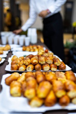 Bir açık büfe masasında tepsilerde çeşitli taze pişmiş hamur işleri düzenlenir. Katılımcılar yakınlarda toplanır, şirket toplantılarının tadını çıkarırlar..