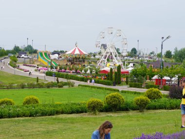 Bereketli bir lunapark, dönme dolap, atlı karınca ve yemyeşil çiçeklerle çevrili renkli slaytlar.