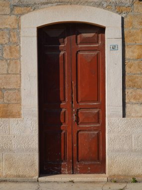 Kırsal taştan bir duvarda boyası soyulmuş, açık renkli taş kemer çerçeveli klasik ahşap kapı.. 