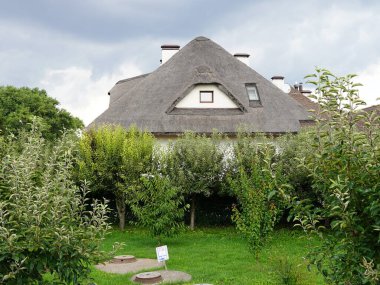 Büyüleyici bir kır evi geleneksel sazdan çatılı, yemyeşil ağaçların ve meyve bahçesinin arasına kurulmuş.