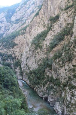 Derin bir kanyonun nefes kesen manzarası. Yüksek uçurumlar ve yemyeşil sularda süzülen bir turkuaz nehri..
