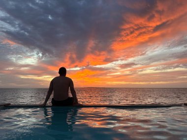 Adam maldivlerdeki villasında havuz kenarında otururken inanılmaz gün batımını seyrediyor. Yüksek kalite fotoğraf