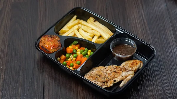 food package menu of chicken steak, potatoes and vegetables on dark background. additional tomatoes and barbecue sauce