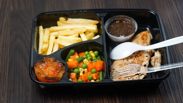 food package menu of chicken steak, potatoes and vegetables on dark background. additional tomatoes and barbecue sauce