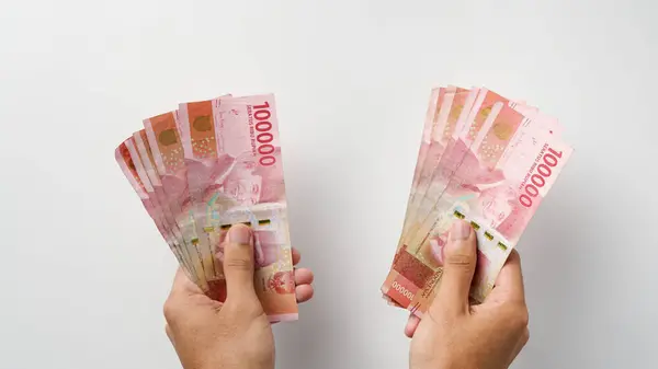 Both hands hold Indonesian rupiah notes. Indonesian currency