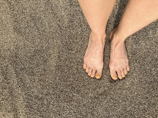 一个有黄色指甲油的女人的腿在沙子的背景下 柔和的落日光芒 顶部的景色 — 图库照片