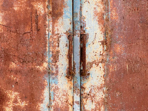 Fabrikadaki eski paslı metal kapılar kapalı. Kırmızı-turuncu paslı tüplerden yapılmış uzun sapları kapatın. Kaplama kıyafeti. Ön görünüm