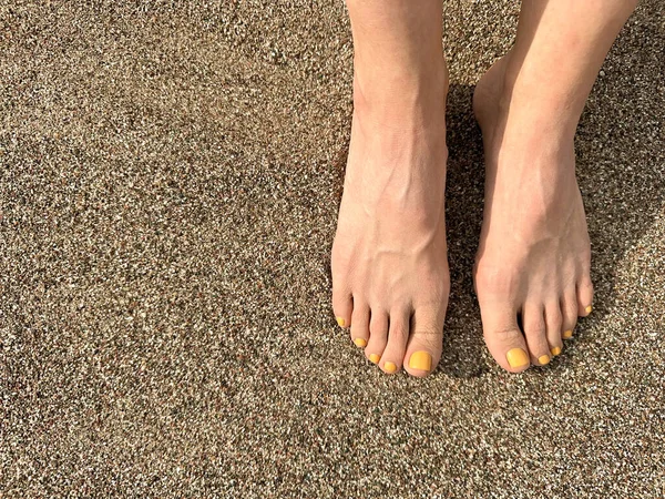 The girl put her feet together on the sand in a golden sunset. Yellow nail polish on her toes. Top view, free space for your text, close up
