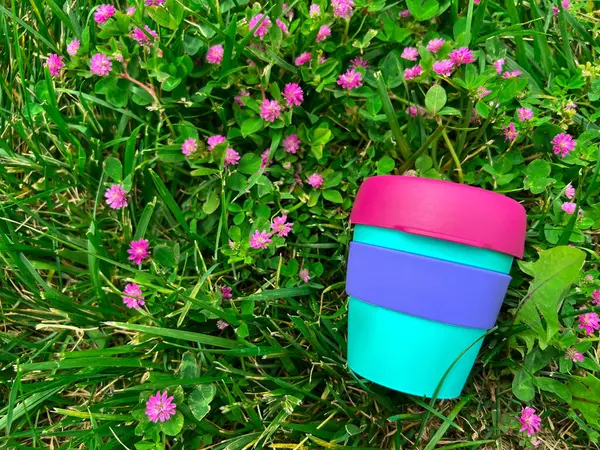 Élénk Újrahasznosítható Műanyag Ital Csésze Füvön Rózsaszín Virágokkal Közelről — Stock Fotó