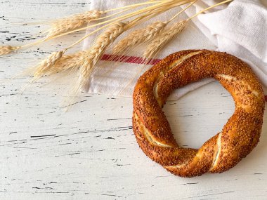 Geleneksel Türk hamur işi simit masada yatıyor. Buğday çivileri ve kırmızı çizgili beyaz mutfak havlusunun yanında. Yukarıdan görüntüle