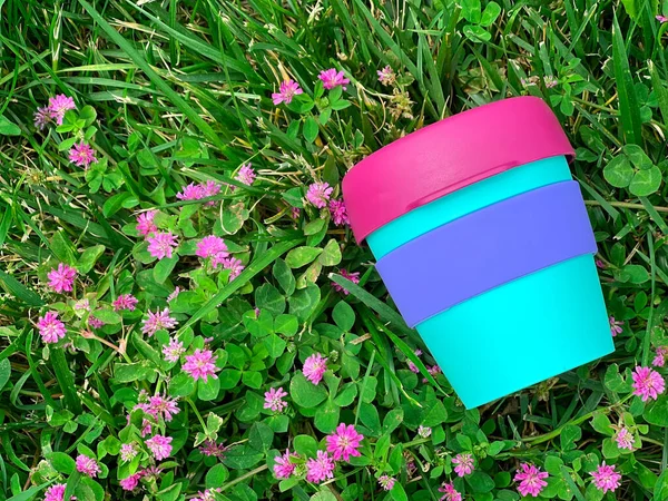 ピンクの花と芝生の上で明るい再利用可能なプラスチック飲料カップ 近いビュー — ストック写真