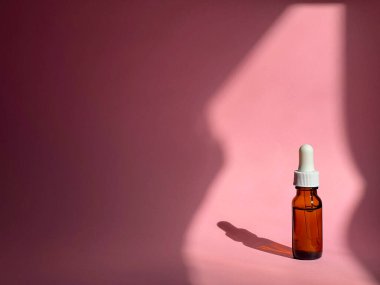 Üzerinde güneş ışığı olan pembe bir zemin üzerinde serum bulunan şeffaf kozmetik kavanoz. Güzellik rutini. Cilt bakımı