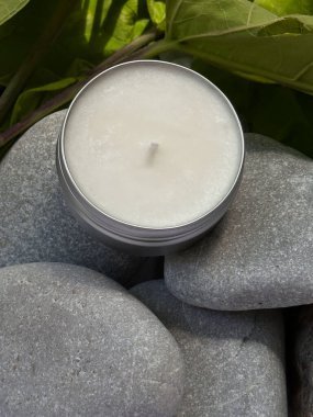 Soya mumundan yapılmış beyaz yuvarlak mum bir taş ve yeşil yaprakların üzerinde yatar. Durgun hayat