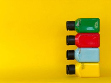 Sarı arka planda parlak renkli akrilik boyalı dört şişe. Yeşil, mavi, kırmızı, sarı