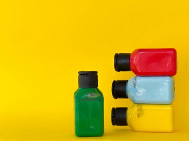 Sarı arka planda parlak renkli akrilik boyalı dört kavanoz. Yeşil, mavi, kırmızı, sarı