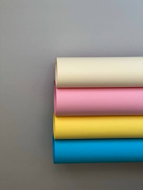 Basit gri bir arkaplanda 4 rulo renkli kağıt. Sarı, mavi, bej, pembe