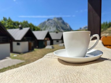 Terasta muhteşem manzaralı beyaz bir kupa. Dağlar, blu gökyüzü ve küçük evler