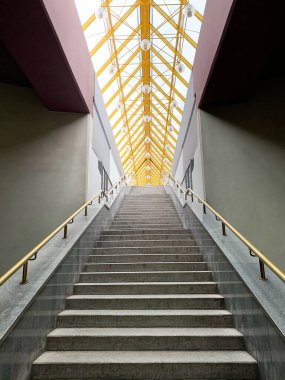 Cam çatının altında sarı tırabzanlar olan gri merdivenler. Simetrik resim, aşağıdan görünüm, modern mimari
