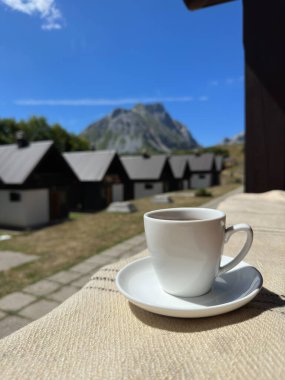 Pencere pervazında beyaz bir kupa. Dağ ve köy manzarası. 