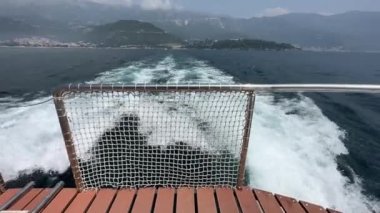 Tekneden gelen izler, parlak mavi okyanusta beyaz dalgalar dağ kitlelerinin arka planına karşı. Deniz gezisi başlıyor, manzara.