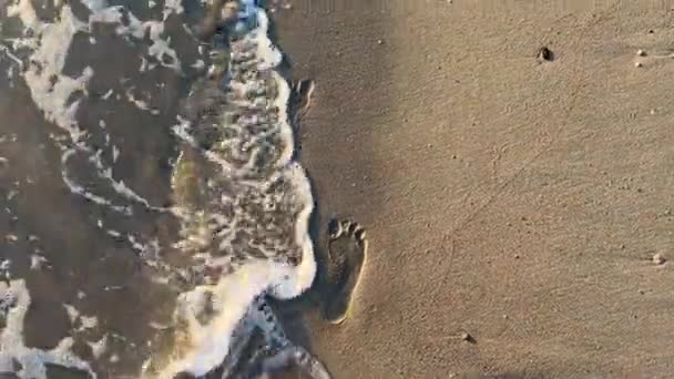 海のサーフィンの波が砂の上の人の足跡を洗い流します 上からの眺め 海岸の美学 — ストック動画