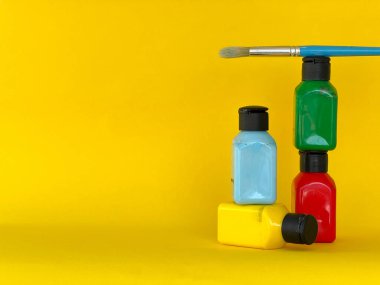 Dört kavanoz, parlak renkli akrilik boya ve sarı arka planda boya fırçası. Yeşil, mavi, kırmızı, sarı