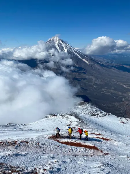 Group of tourists climb to the snow mountain top. Small figures of people in colourful clothes against the majestic mountains