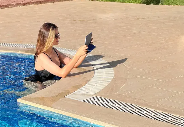 Freelancer girl works out of the pool. Side view, bright natural lighting, girl uses tablet