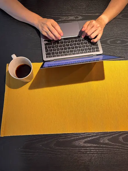 Flat lay: the developers hands are on the keyboard, next to the coffee mug. Against the background of a dark wood table and a bright orange tablecloth