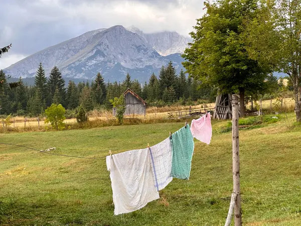 Fresh clothes dry on a rope in the yard. Against the background you can see mountains, conifer forest and sky with clouds
