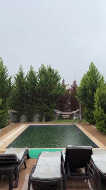 Avluda büyük yağmur damlaları ve yüzme havuzlu dikey video. Yeşil gölgeli çerçeve