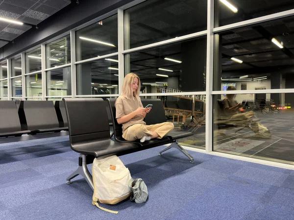 Long-term transplant at the airport. Girl sits in an empty departure waiting room and watches viral content in phone