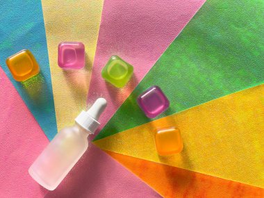 Çok renkli bir arka planda serum şişesi. Şeffaf buz küpleri, renkli gölgeler
