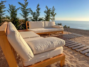 Uçurumun kenarındaki beyaz kanepeler ve panoramik deniz manzaralı dinlenme alanı..