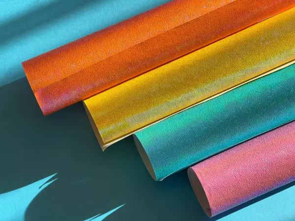 Rolls of shiny colored paper on a blue background. Lights and shadows