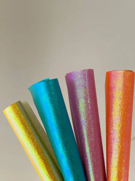Rolls of shiny colored paper against the simple beige background.