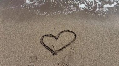 Islak kumda kalp şeklinde çizimler, kıyıda dalgalar, aşk konsepti.