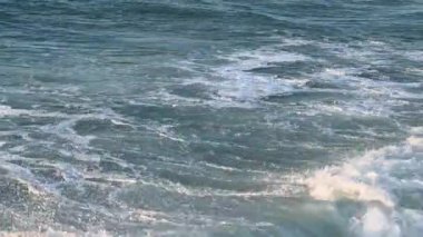 Turuncu bir günbatımının arka planında bol köpüklü fırtına dalgaları.