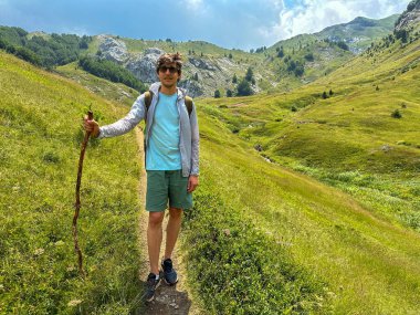 Çimenli dağ arazisinde yürürken tahta bir değnek tutan yürüyüşçü..