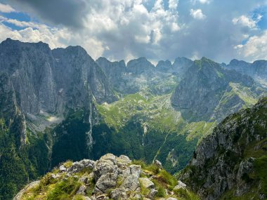 Bulutlu bir gökyüzünün altında sivri tepeleri olan nefes kesici bir dağ sırası..