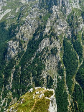 Dik dağ uçurumları kayalık oluşumlar ve aşağısı yeşil orman örtüsüyle kaplı..