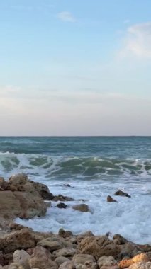 Gün batımında dalgalar çakıllı bir sahile yavaşça çarpıyor..