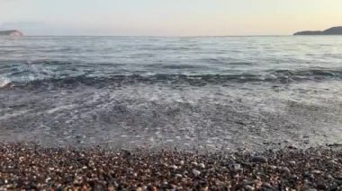 Yumuşak bir akşam gökyüzünün altında kayalık bir sahilde okyanus dalgaları kırılıyor..