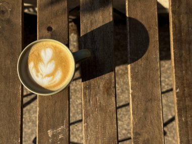 Bir bardak kremalı latte köpüklü sanat eseri sade ahşap bir masada oturuyor..