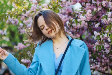 İlkbaharda çiçek açan kiraz ağacında poz veren güzel bir kadın. Baharda çiçek açan bir bahçede güzel bir kızın portresi. Tatmin ve sükunet duyguları. Kapalı gözlü mutlu bir kadın..