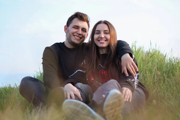 幸せな若いカップルの愛 人々はカメラを見て カップルは草の上に座っています 抱擁とロマンス 本当の感情 幸福と喜び 自然の中でロマンチックなデート — ストック写真